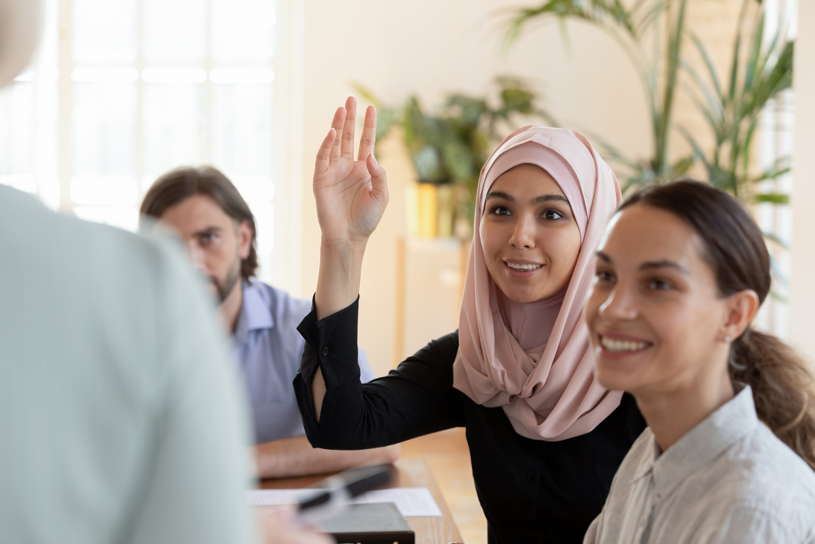 Smiling asian muslim businesswoman raise hand ask question at seminar